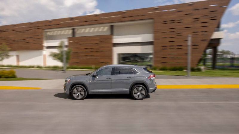 Camioneta Cross Sport 2025 de Volkswagen en color gris circula frente a edificio moderno.