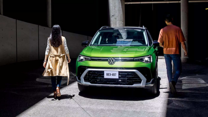 VW Taos. Vista frontal de camioneta SUV de color verde en estacionamiento oscuro con pareja caminando.