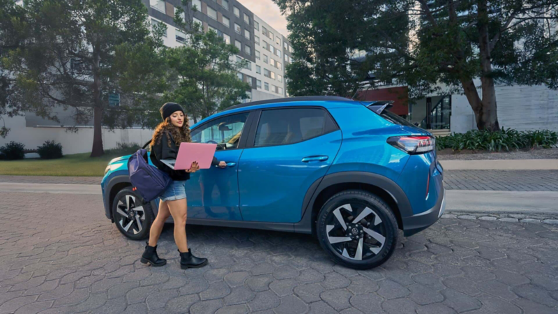 Mujer camina con laptop rosa junto a Volkswagen Tera 2026.