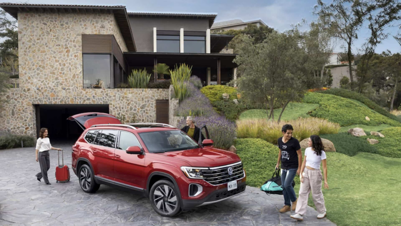 Camioneta Teramont 2025 en color rojo a las afueras de una casa moderna y familia que sube equipaje a cajuela.