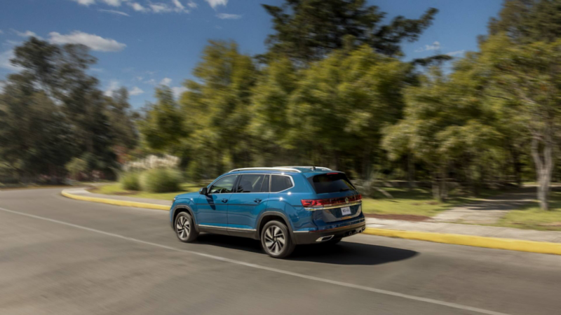 Volkswagen Teramont azul circula por camino rodeado de árboles.