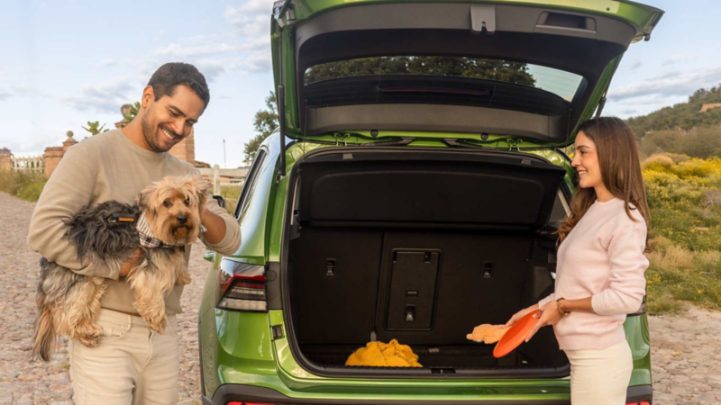 Pareja guarda equipaje en la cajuela de una SUV Taos de color verde, mientras el hombre carga a su perro.
