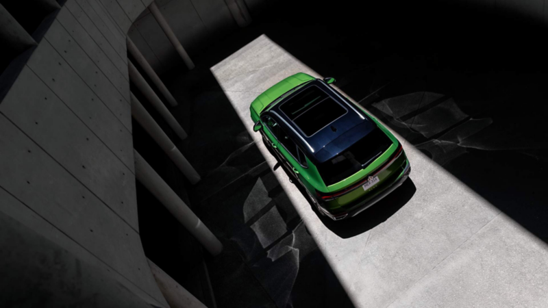 Taos de Volkswagen verde con techo panorámico, visto desde arriba entre sombras de edificios oscuros.