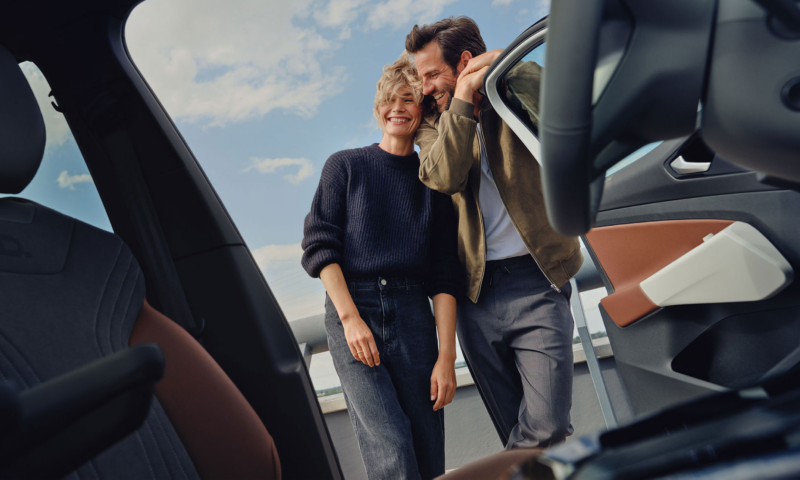 Una pareja sonriendo vistos desde el interior de un Volkswagen con la puerta abierta