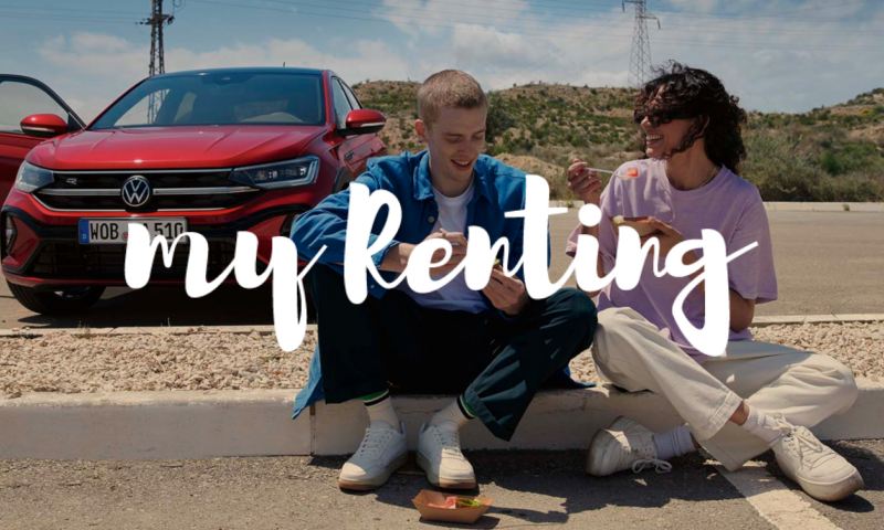 Una pareja sentada en un bordillo delante de un Volkswagen con el logo de My Renting