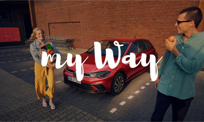 Un hombre y una mujer al lado de un Volkswagen de color rojo con el logo my way