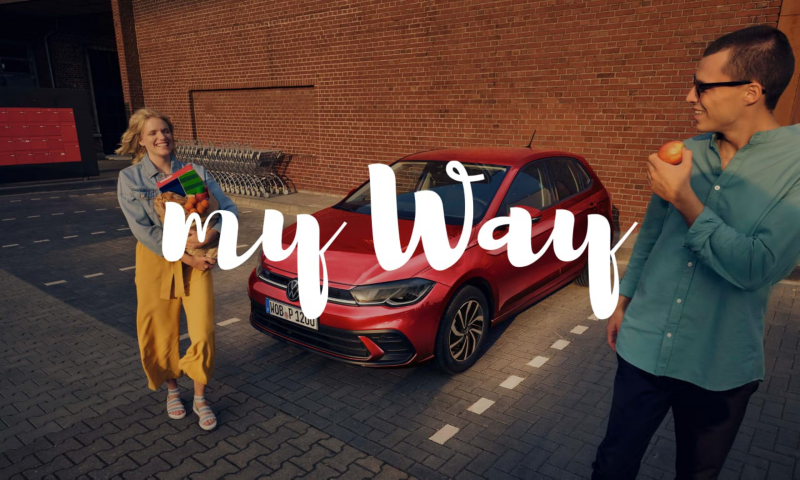 Una pareja delante de un Volkswagen de color rojo estacionado con el logo de my way