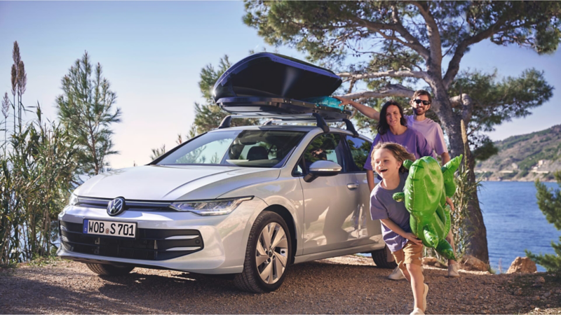 Una familia frente al mar junto a un Volkswagen con un baúl en el techo