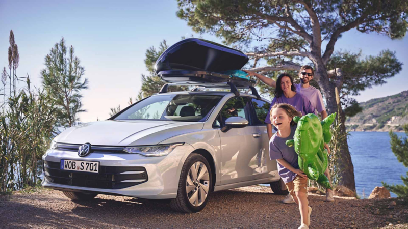 Una familia feliz sacando objetos del cofre de techo de un Volkswagen