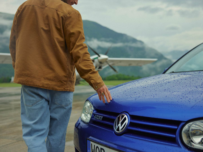 Un hombre caminando delante de un Volkswagen Golf azul