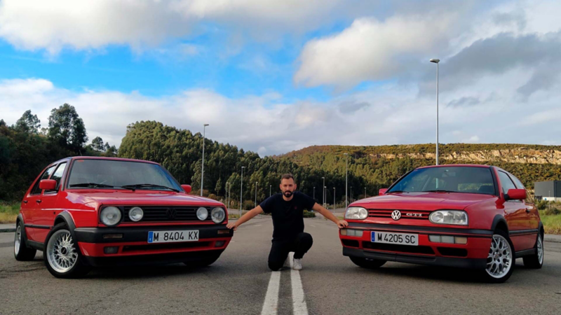 Rodrigo entre medias del Golf rojo clásico de su madre y su Golf GTI 20 Aniversario también rojo aparcados al aire libre con bosques de fondo