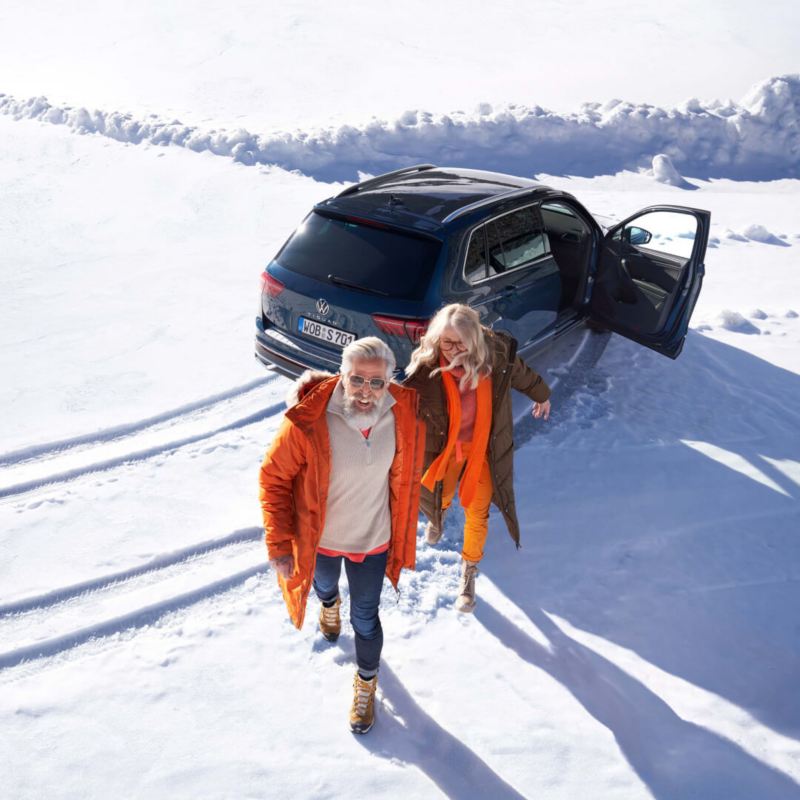 Una pareja junto a un Volkswagen SUV con la puerta abierta en la nieve