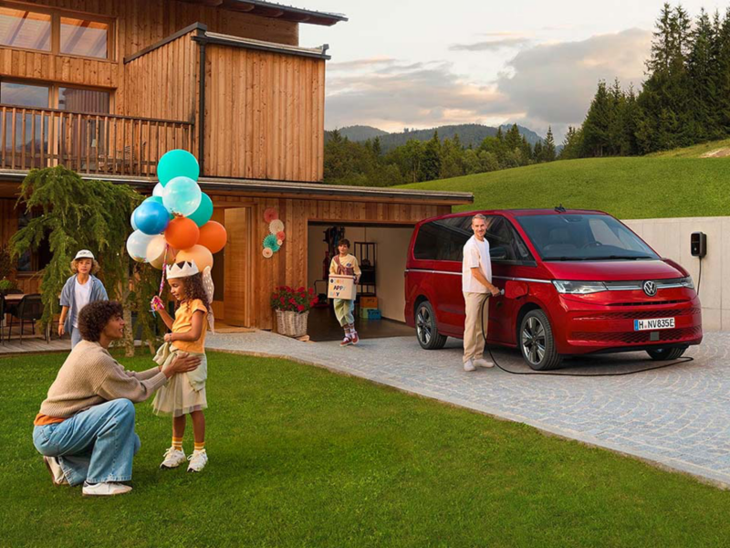 Una furgo Volkswagen familiar aparcada en la puerta de una casa con personas alrededor celebrando un cumpleaños