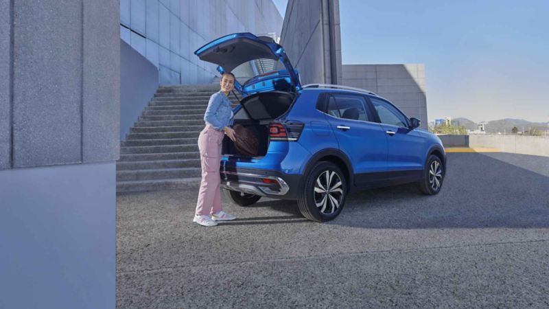 Mujer mete maleta en la cajuela de Volkswagen Taigun, camioneta SUV en color azul.