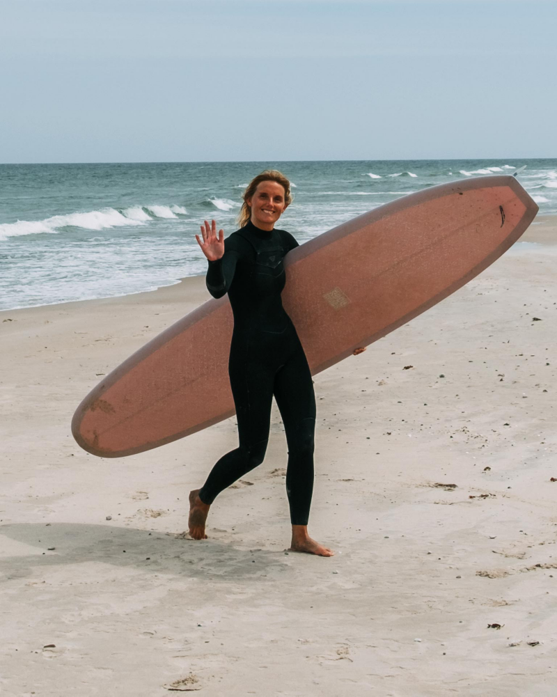 Caroline springer på stranden med en surfbräda på Gotland.