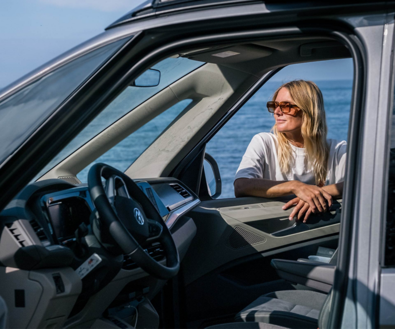 Vy genom framsätet i VW California med Caroline lutad mot den öppna dörren.