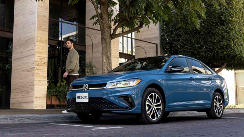 Auto sedán Jetta de Volkswagen en color azul estacionado a las afueras de un edificio moderno.