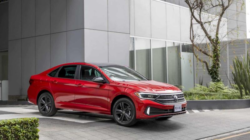 Volkswagen sedán de color rojo sale del área de pick up de un edificio moderno.