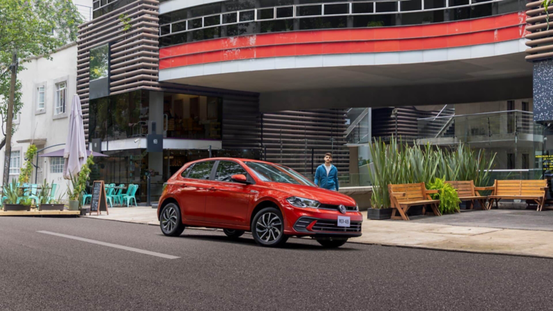 Polo Volkswagen de color rojo a las afueras de un edificio, con joven que camina hacia el subcompacto. 