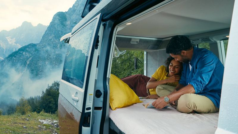 A couple relaxing inside a VW California parked next to a mountainside.
