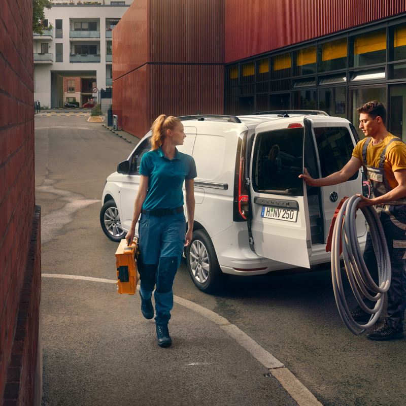 A white Caddy Cargo delivery van is parked outside a building with tradespeople