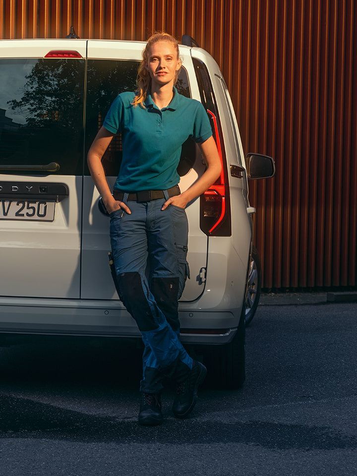 Eine Frau lehnt an die Heckflügeltüren des Volkswagen Caddy Cargo.