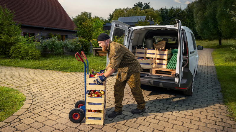 Ein Obstbauer lädt sein Obst aus einem VW Caddy Flexible auf einen Pritschenwagen.