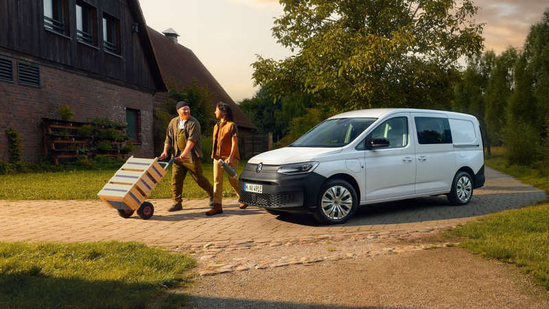 Zwei Personen gehen von Caddy Flexible weg, wobei einer der beiden eine Sackkarre mit drei Kisten vor sich herschiebt.