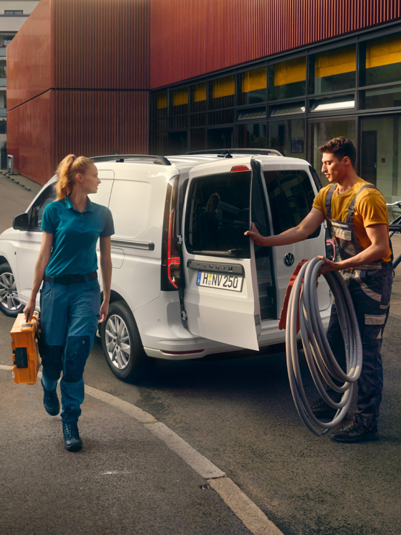 Zwei Handwerker laden ihr Material und Werkzeug aus dem VW Caddy Cargo.