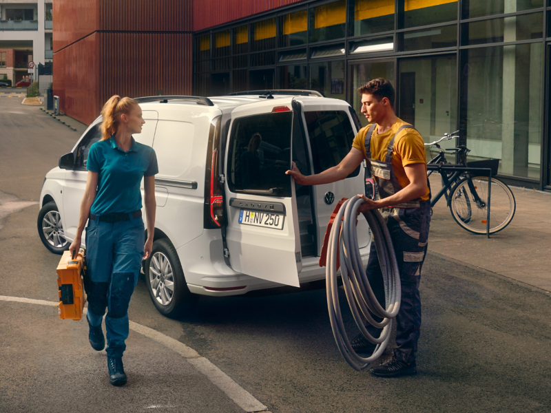 Zwei Handwerker laden ihr Material und Werkzeug aus dem VW Caddy Cargo.