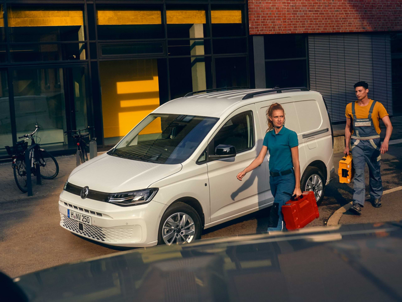 Handwerker vor einem weißem VW Caddy Cargo welcher vor einem Gewerbegebäude parkt