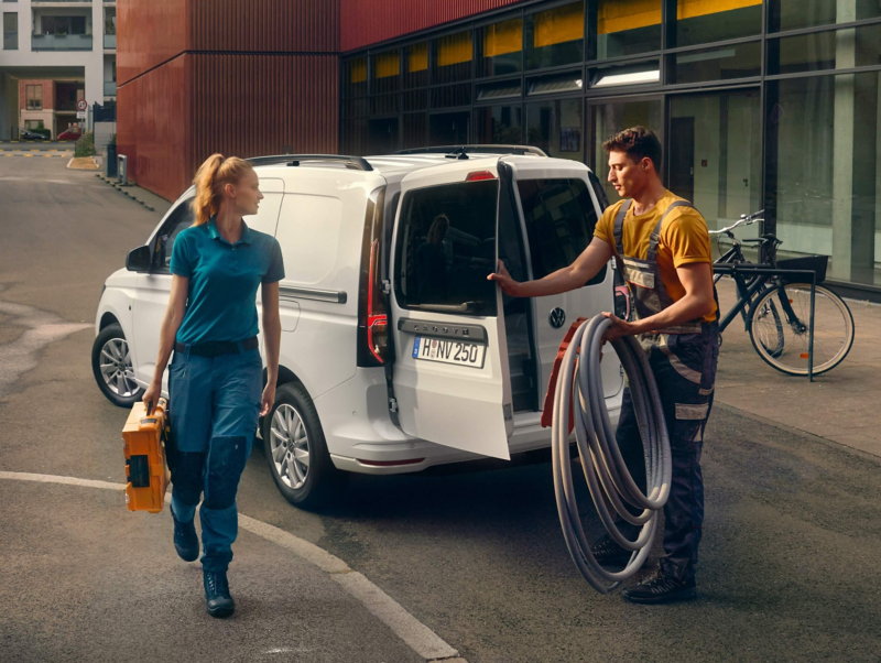 Zwei Handwerker laden ihr Material und Werkzeug aus dem VW Caddy Cargo.