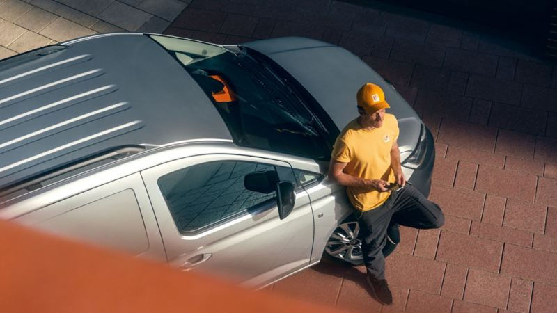 Un uomo con in mano uno smartphone è appoggiato su Caddy Cargo Volkswagen, visto dall'alto.