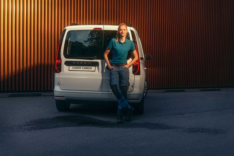 Kobieta opierająca się o tylne drzwi skrzydłowe nowego Volkswagena Caddy Cargo.