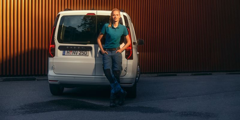 Eine Frau lehnt an die Heckflügeltüren des neuen Volkswagen Caddy Cargo.