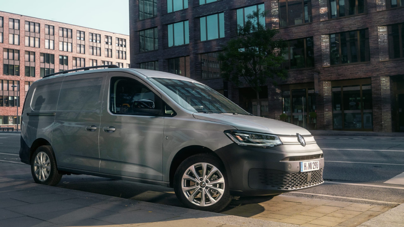 Ein grauer VW Caddy Kombi parkt am Straßenrand vor einem modernen Bürokomplex.