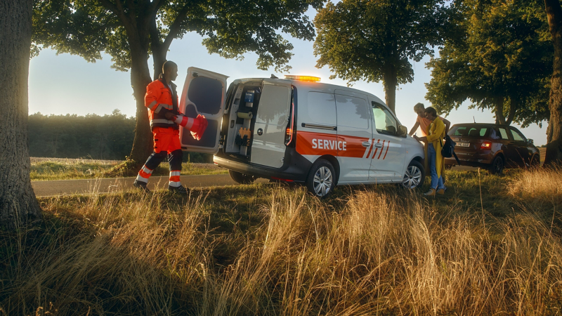 Ein VW Nutzfahrzeug Service Mobil steht am Straßenrand und hilft einem liegengebliebenen Pärchen..