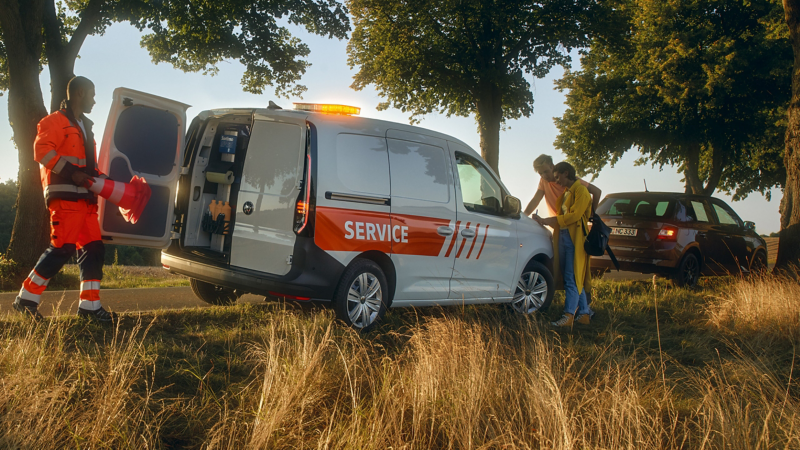 Pojazd serwisowy Volkswagen jest zaparkowany na poboczu i trwa udzielanie pomocy.