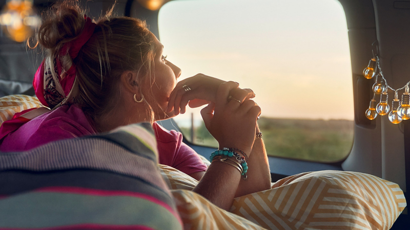 Eine Frau die in einem Bett des VW Caddy liegt.