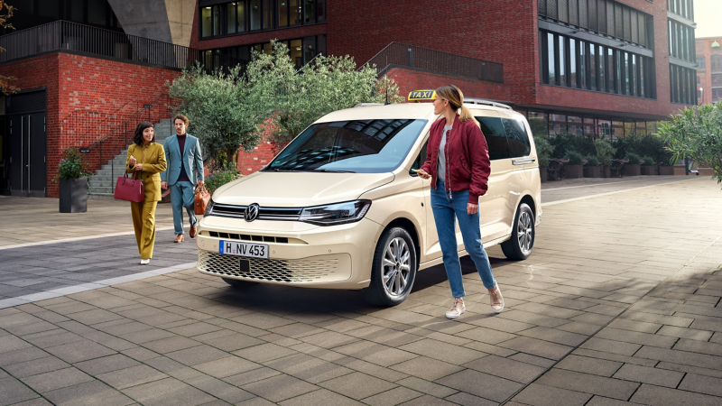 Ein VW Caddy mit Taxi-Umbau parkt vor einem modernen Backsteingebäude