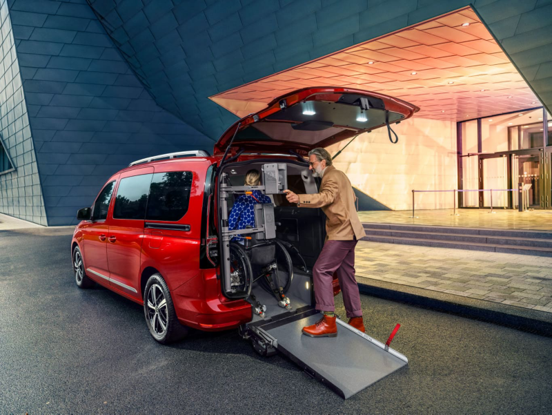 Mężczyzna umiejscawia kobietę na wózku inwalidzkim w Volkswagenie Caddy za pomocą rampy.