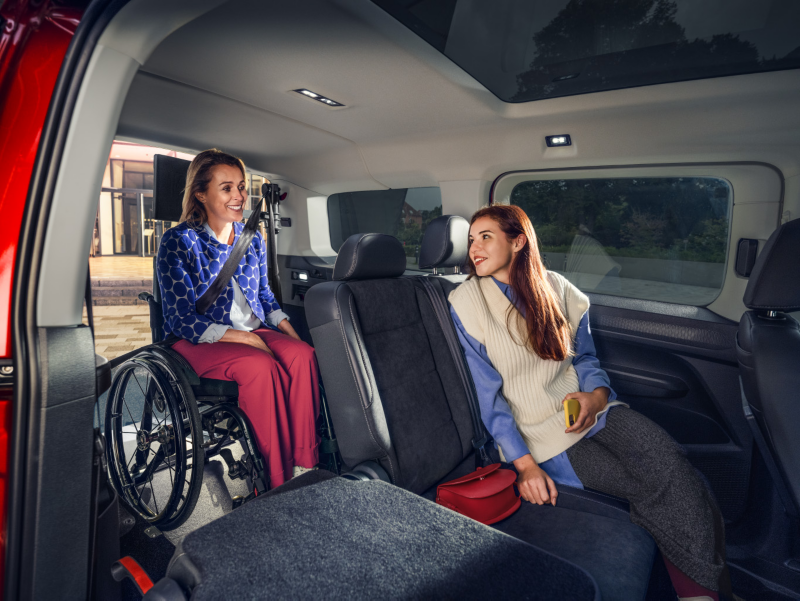 Kobieta na wózku inwalidzkim rozmawia z kobietą siedzącą na tylnym siedzeniu wewnątrz Volkswagena Caddy.
