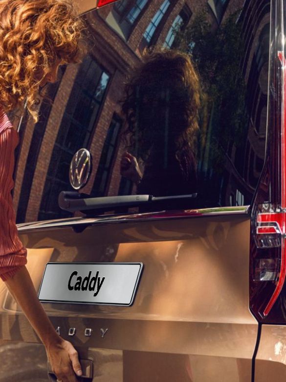 Eine Frau öffnet die Heckklappe des VW Caddy.