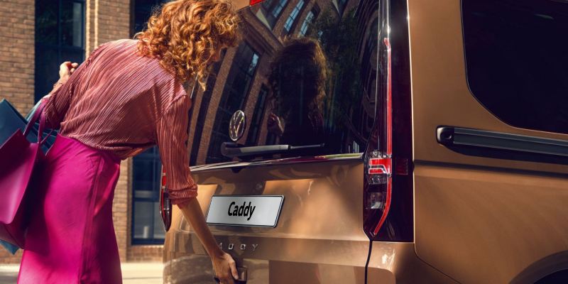 Eine Frau öffnet die Heckklappe des VW Caddy.