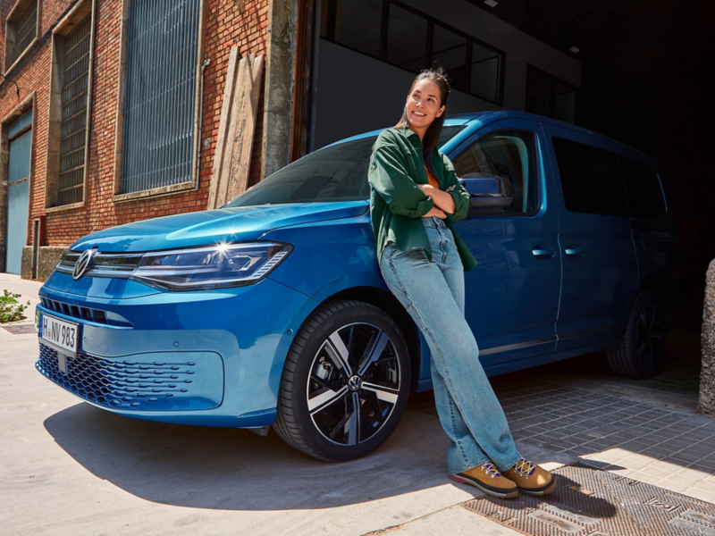 Eine Person lehnt sich gegen einen blauen VW Caddy welcher am Tor einer Lagerhalle steht