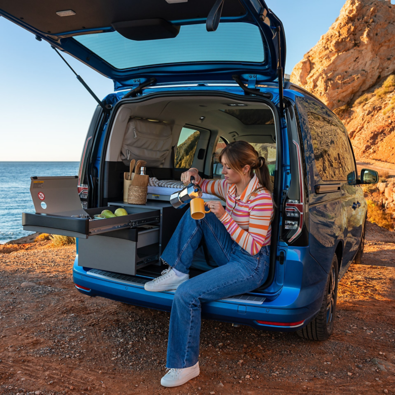 En kvinna häller upp kaffe i bakluckan på en VW Caddy California.