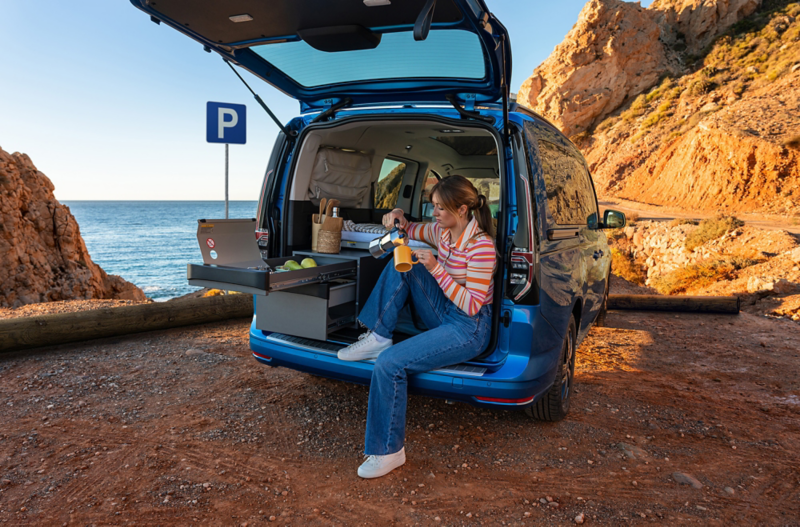 Une femme se sert un café assise dans le VW Caddy California.