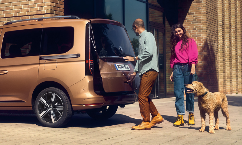 Der VW Caddy im Anschnitt seitlich von hinten in der ein Mann den Kofferaum öffnet.