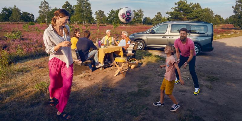 En familj kickar boll och fikar runt en VW Caddy Maxi familjebil