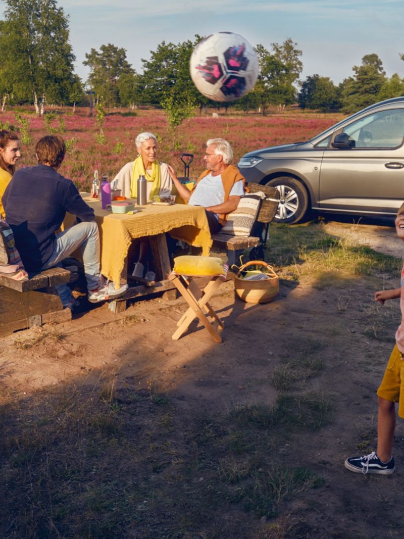 En familj kickar boll och fikar runt en VW Caddy Maxi familjebil